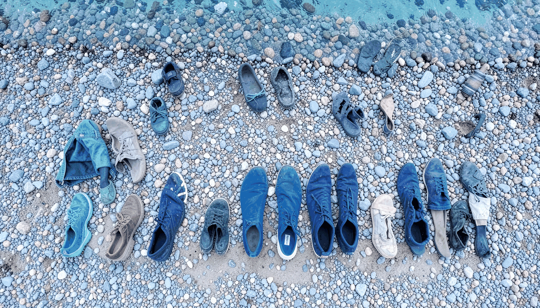 Derive giovanili allineate su una spiaggia di ciottoli grigi con acqua turchese sullo sfondo, in una luminosa giornata di sole