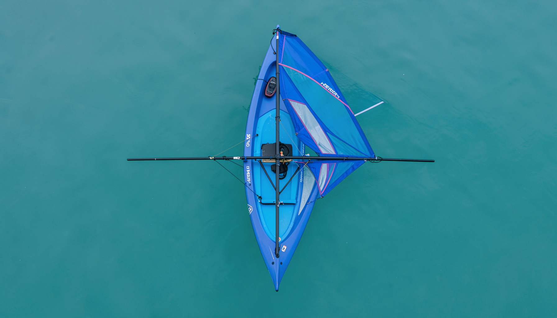 Tavola a vela Techno 293 con vela colorata su sfondo di acqua verde-blu, composizione dall'alto